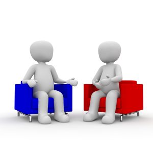 zdjęcie przedstawia dwie postacie, siedzące na fotelach i rozmawiające ze sobą